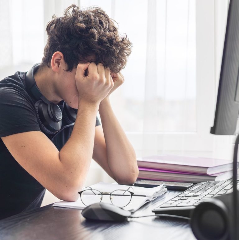 Wenn Buchstaben keinen Sinn ergeben Junger Mann mit Händen im Gesicht, frustriert am Schreibtisch vor Computer.