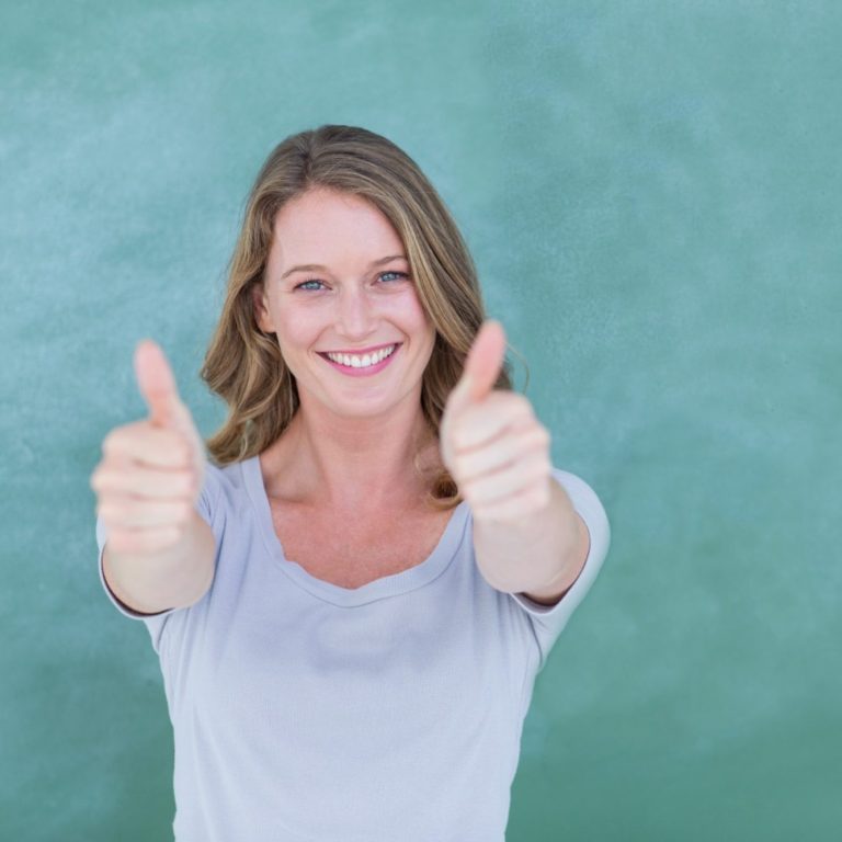 Nachhilfe-Tutorin Lächelnde Frau, eine Lehrerin, steht mit Daumen nach oben vor einer grünen Tafel