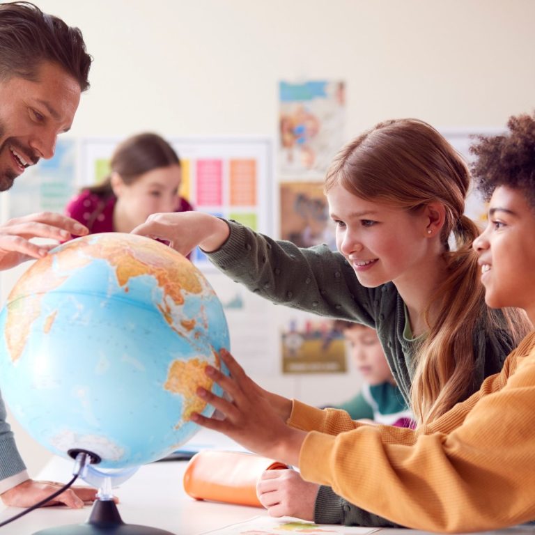 Unterricht in kleiner Lerngruppe Eine Gruppe von Kindern und einem Lehrer erkundet einen Globus.